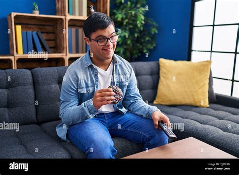 Down syndrome man watching tv eating doughnut at home Stock Photo - Alamy