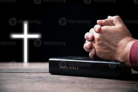 Hands folded in prayer on Holy Bible with cross in church concept for ...