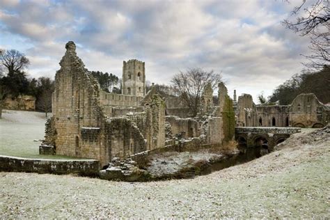 The ruins of Fountains Abbey covered in frost with a cloudy sky in the ...