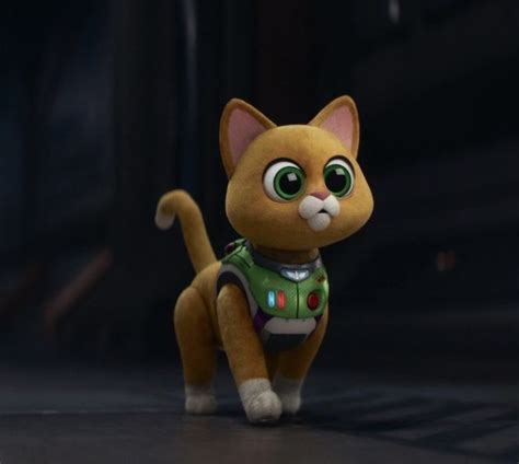 a small toy cat with big eyes and a green vest on it's back