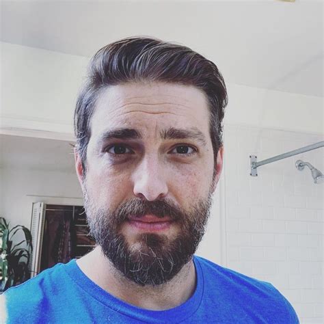 a man with a beard and blue shirt in a bathroom