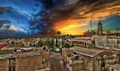 the sun is setting over an old city with tall buildings and clouds in ...