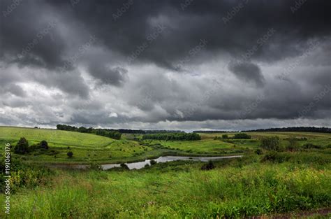 Cloudy summer landscape with small river.Dark stormy clouds in dramatic ...