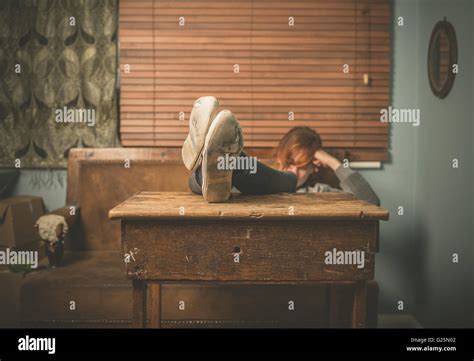 A young woman wearing worn out shoes is resting her feet on a table at ...