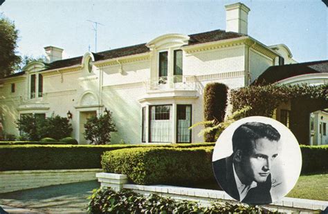 an old photo of a man in front of a white house with hedges and bushes