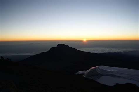 the sun is setting on top of a mountain with clouds in the foreground ...