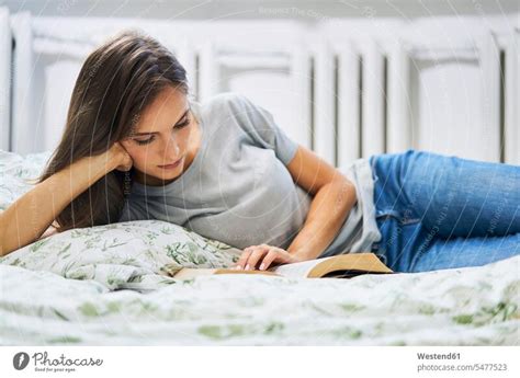 Young woman at home lying in bed reading book - a Royalty Free Stock ...