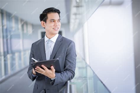 Premium Photo | Young Asian business man holding a tablet looking away