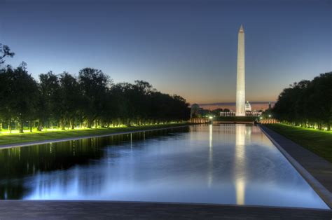 the washington monument is lit up at night with its reflection in the ...