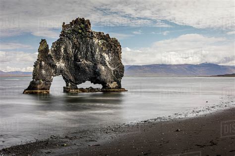 Volcanic rock formation in the shallows on a black sand beach ...