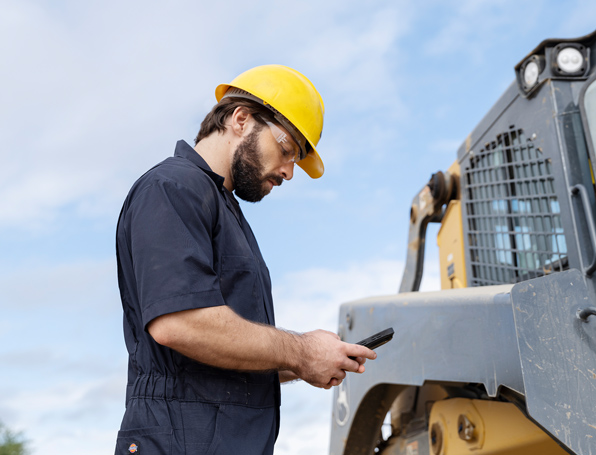 Construction worker standing by construction vehicles, looking at his phone