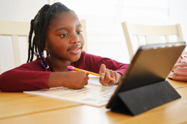 young black girl doing school work at home with a tablet, pencil and paper