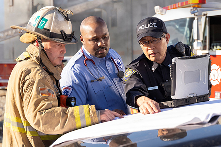 Police officer, firefighter and EMT look at computer while responding to an emergency