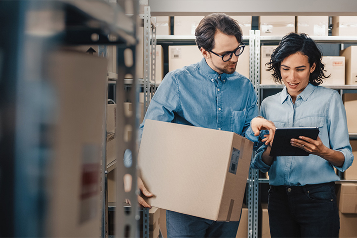 Warehouse workers reviewing order details on tablet while carrying a box