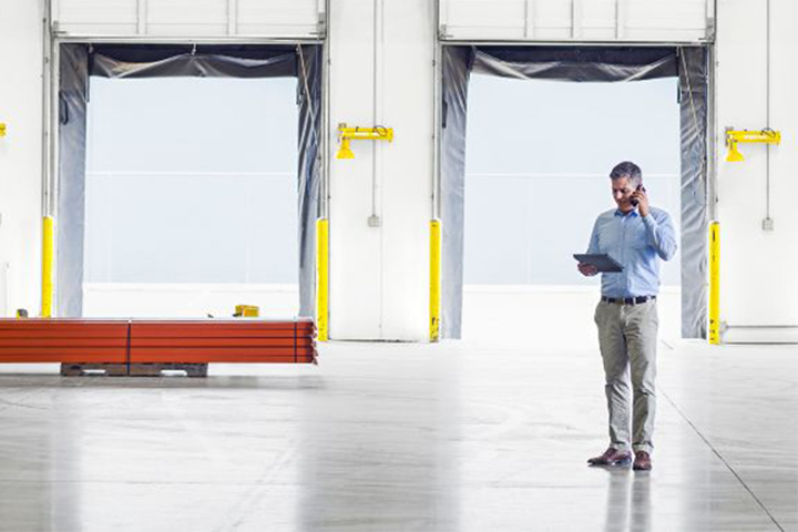 Man talking on phone while reviewing data on tablet in a warehouse