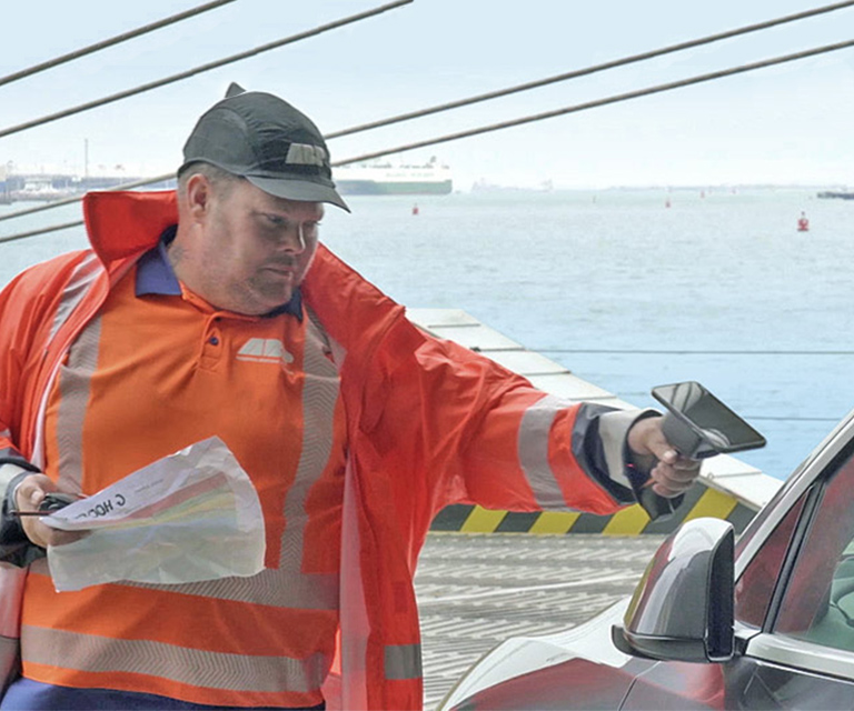 A worker uses a handheld device to scan a vehicle.