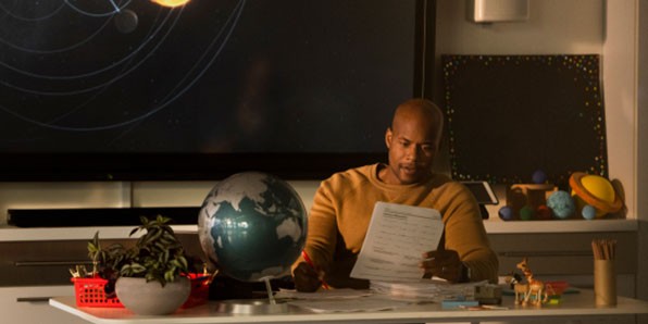 Teacher in classroom grading papers at his desk.