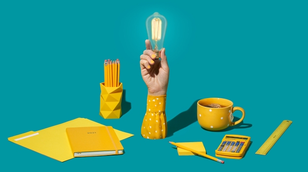 hand holding a light bulb surrounded by work supplies