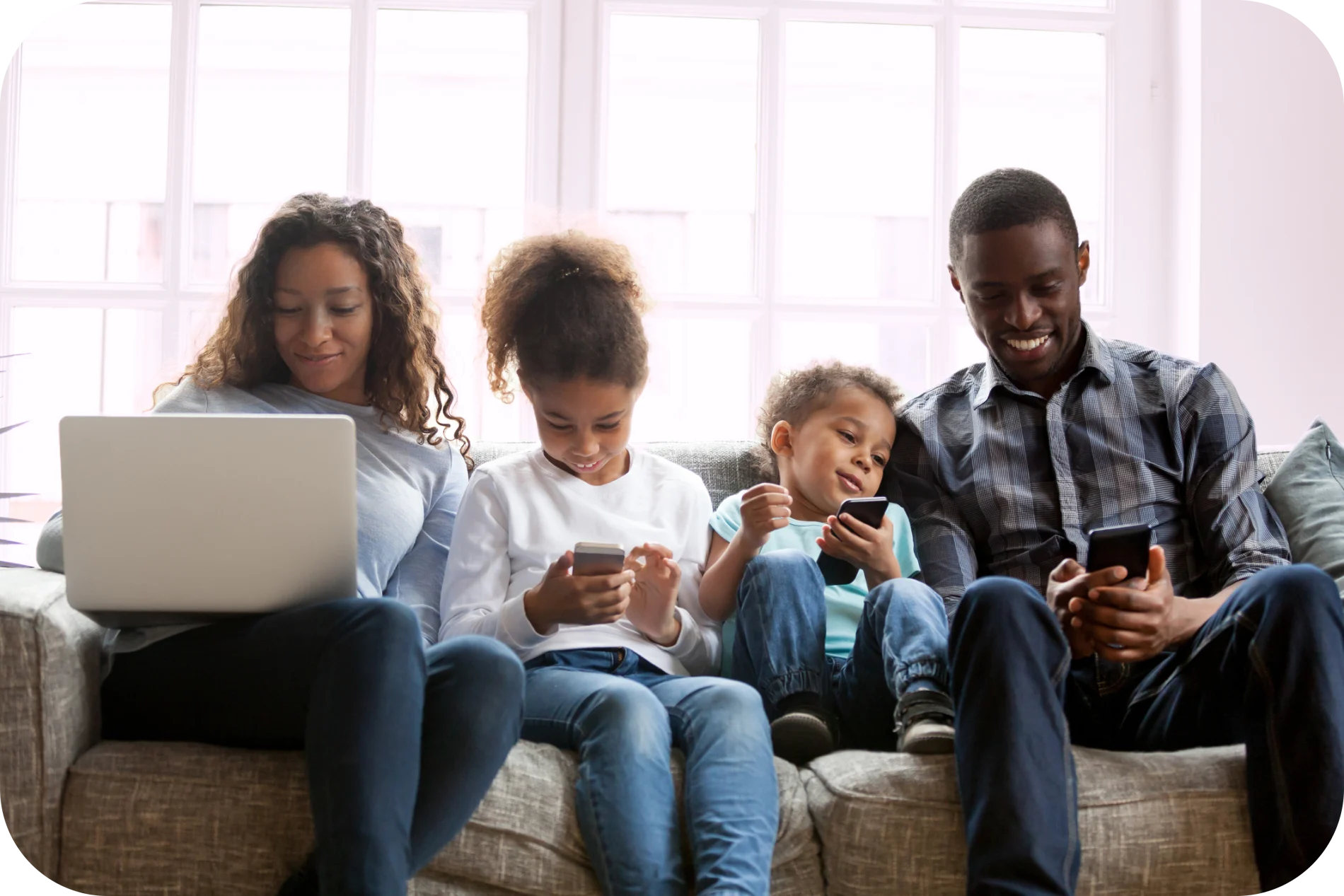 A family of four sitting on the sofa viewing their smartphones and laptop.