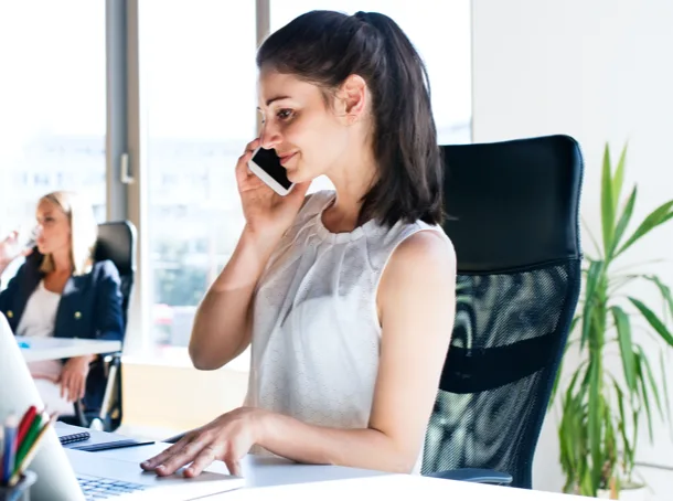 Woman on phone while sitting at desk and working on a computer