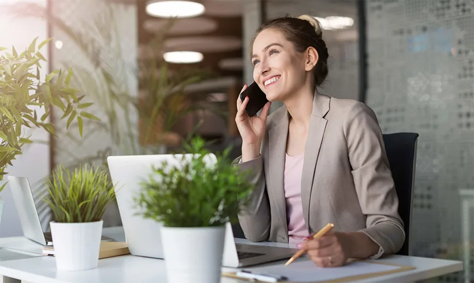 A smiling woman on the phone working at her desk