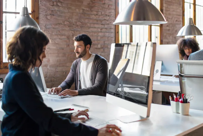 Four individuals working in an open-space office in front of their computers.