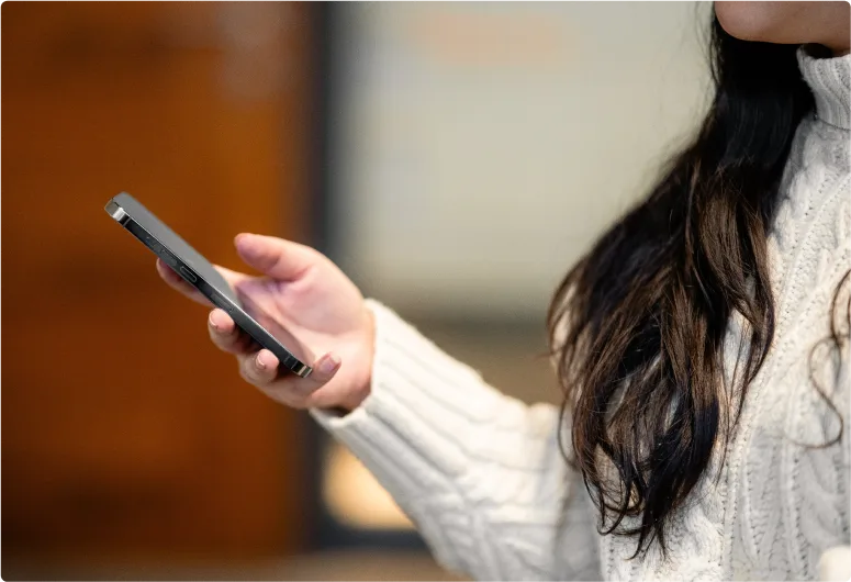 A person’s hands holding a cell phone with a light and bright background.