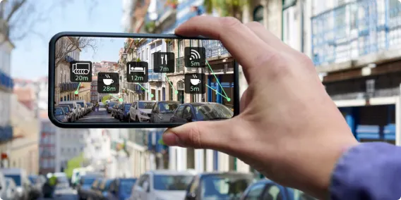 A person’s hand holds a smartphone towards a city street, with the screen displaying icons to indicate nearby businesses and services.