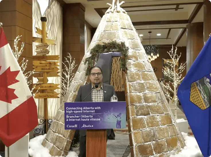 Chief Billy Morin, Enoch Cree Nation, at a podium speaking with Canadian and Alberta flags on each side.