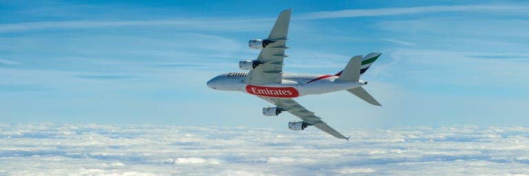 sideview of Emirates Airbus A380 turning right in blue cloudy sky