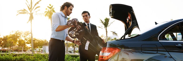 two men fitting golf clubs in car boot