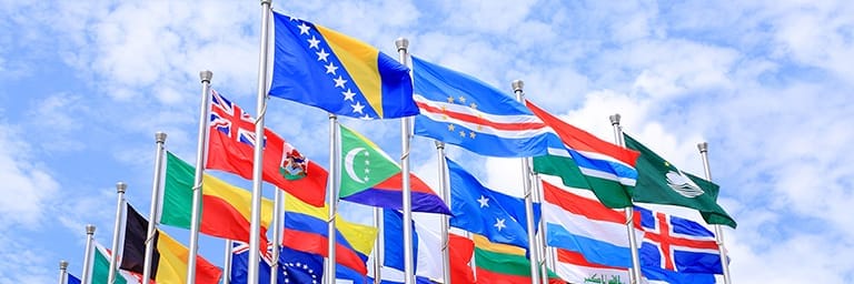 Colourful flags of multiple countries in front of cloudy blue sky