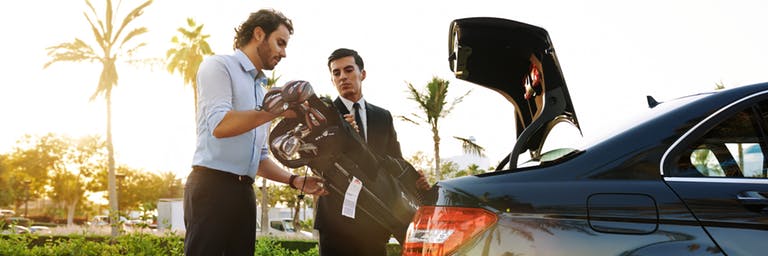 Man putting golf clubs in car trunk