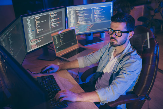 Portrait of his he nice attractive focused brunette guy creating script coding java html mysql database using languages software hard-working at dark room workplace station indoors