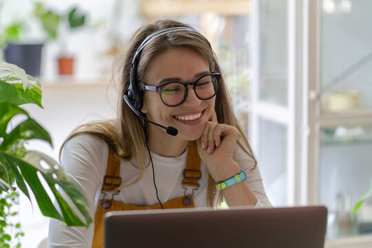 Smiling gardener millennial woman wear headphones talk video calling, using laptop, communicating with clients, watching webinar or video stream conference, remote work from home. Distance education.