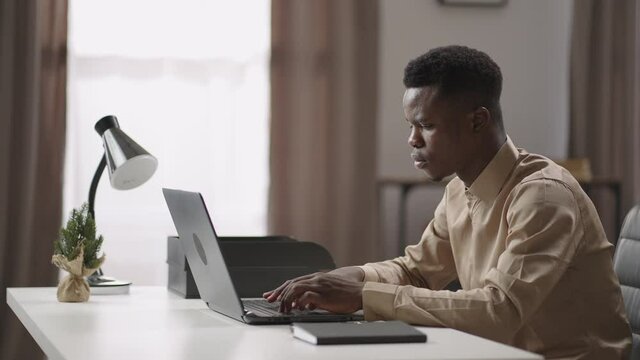 specialist of tech support is working remotely, young black man is sending message in online chat, typing on laptop