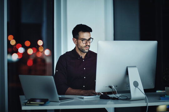 Staying late to get it done. Shot of a young businessman using a computer at his desk during a late night at work.