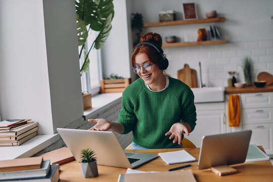 Cheerful young woman in headphones having web conference while working from home