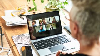 Hybrid work concept image showing man working from home while in a Zoom call with coworkers on laptop.