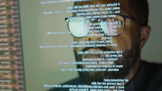 Software developer using python programming language downloaded from the PyPi repository with code reflecting on screen and spectacles.