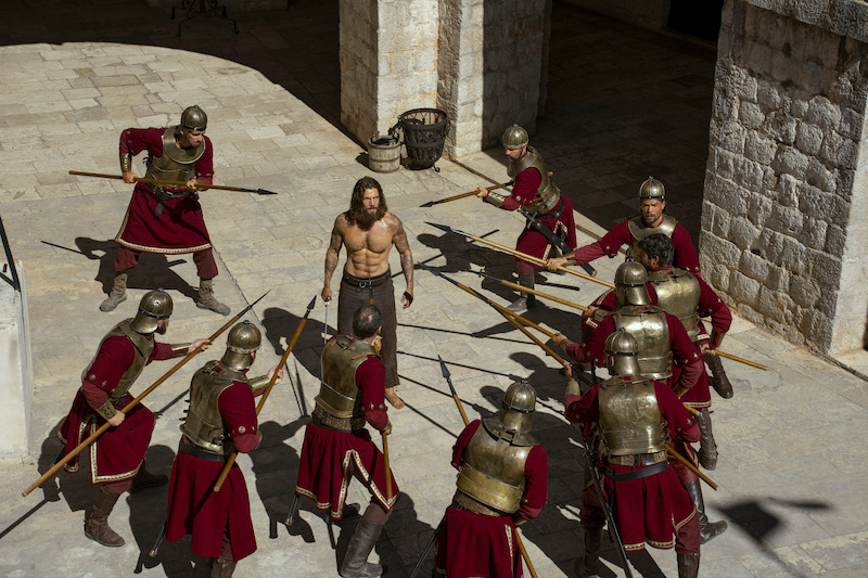 Leo Suter as Harald Sigurdsson surrounded by soldiers pointing spears at him.