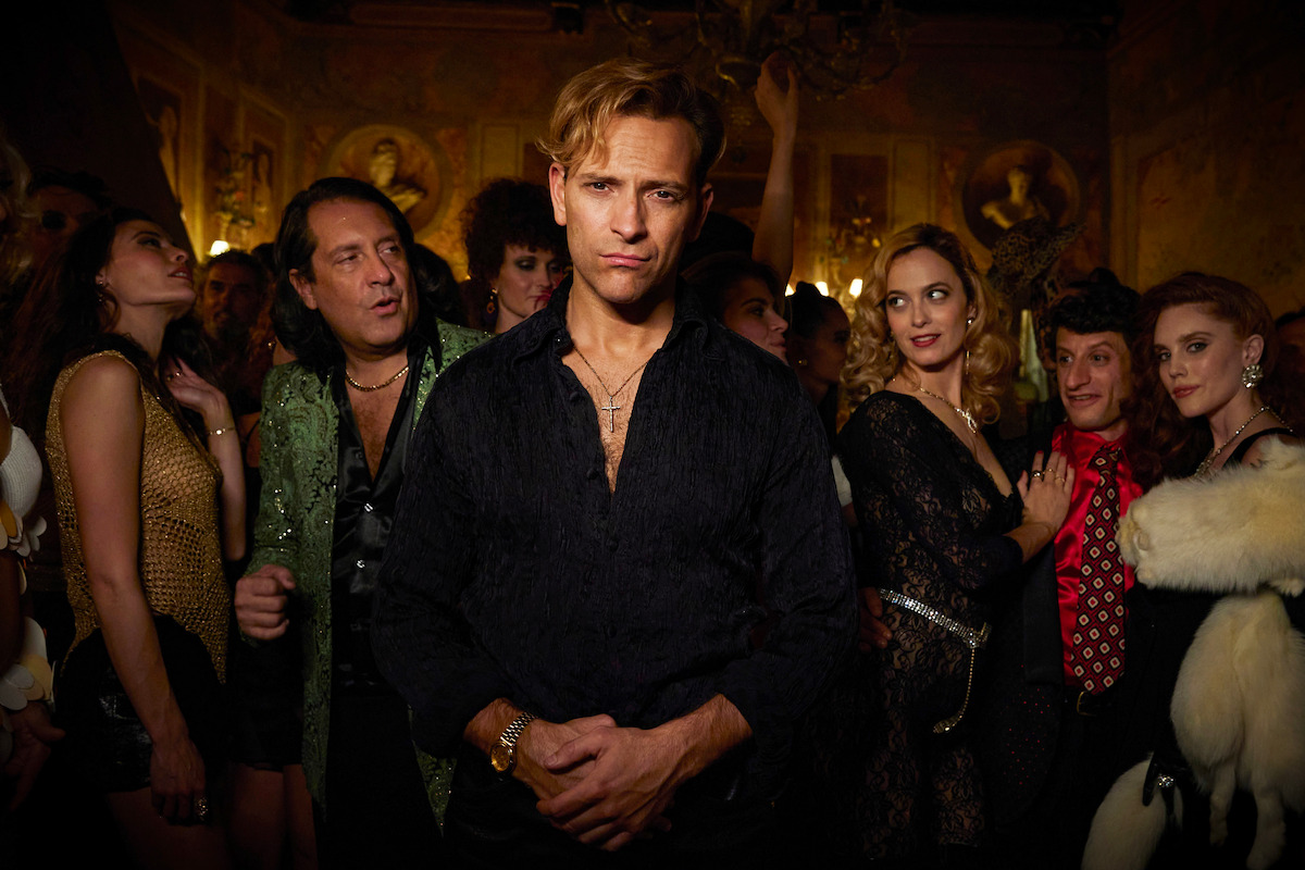 Man in black outfit standing in the middle of a crowd in a nightclub.