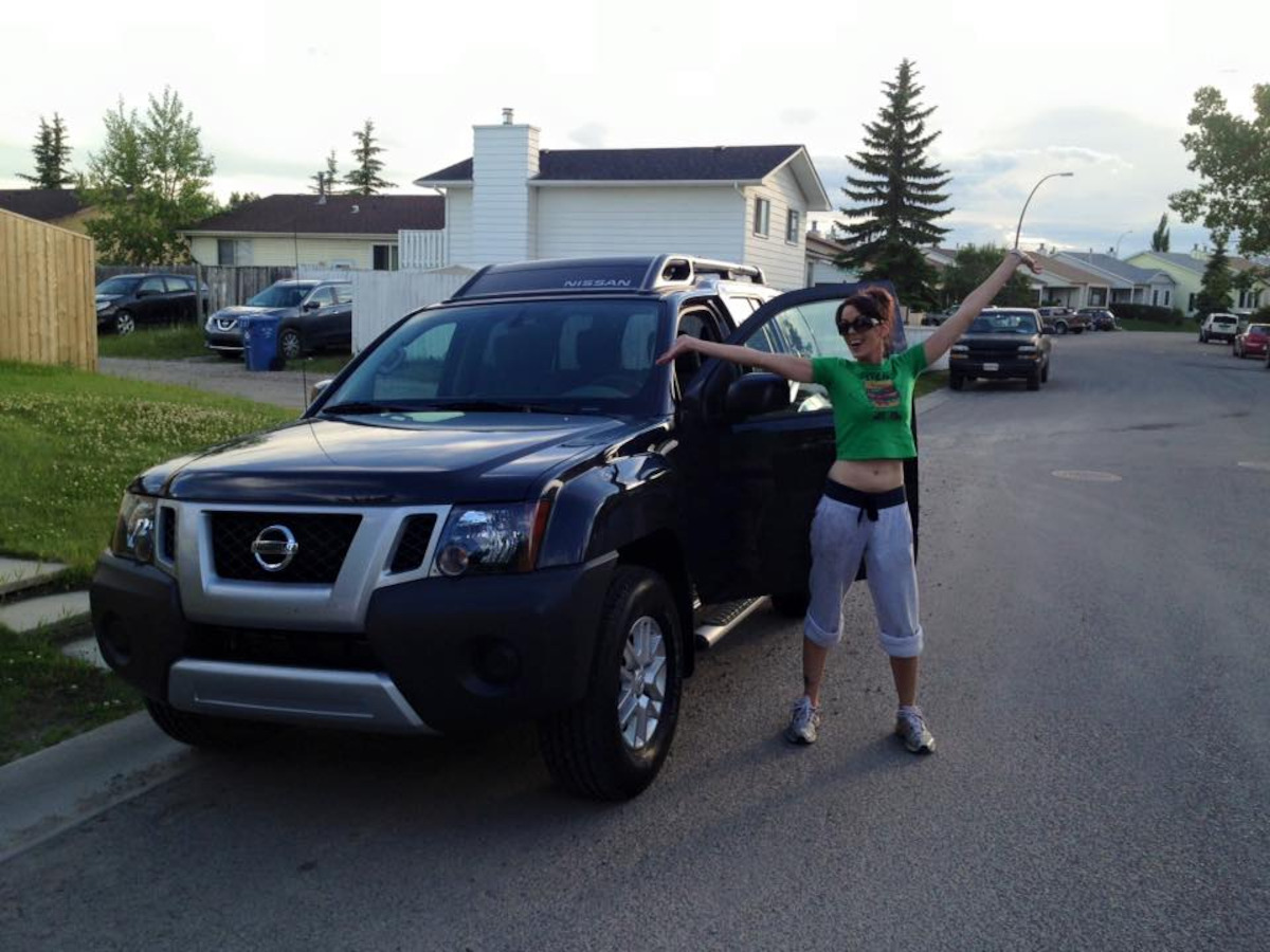 Amanda Antoni smiling with her arms raised next to a car.