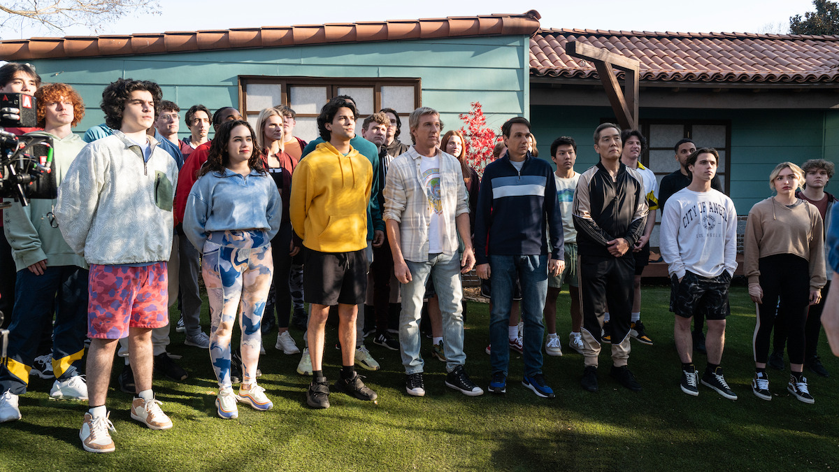 Griffin Santopietro as Anthony LaRusso, Mary Mouser as Samantha LaRusso, Xolo Maridueña as Miguel Diaz, William Zabka as Johnny Lawrence, Ralph Macchio as Daniel LaRusso, Nathaniel Oh as Nate, Yuji Okumoto as Chozen Toguchi, Tanner Buchanan as Robby Keene, Peyton List as Tory Nichols stand together outside of a dojo in Season 6 of ‘Cobra Kai’