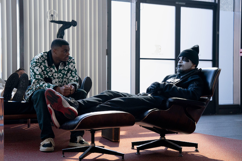 Vince Staples as Vince Staples sits on a couch as Myles Bullock as Bank Robber sits in a recliner chair with his feet up in season 1 of 'The Vince Staples Show'