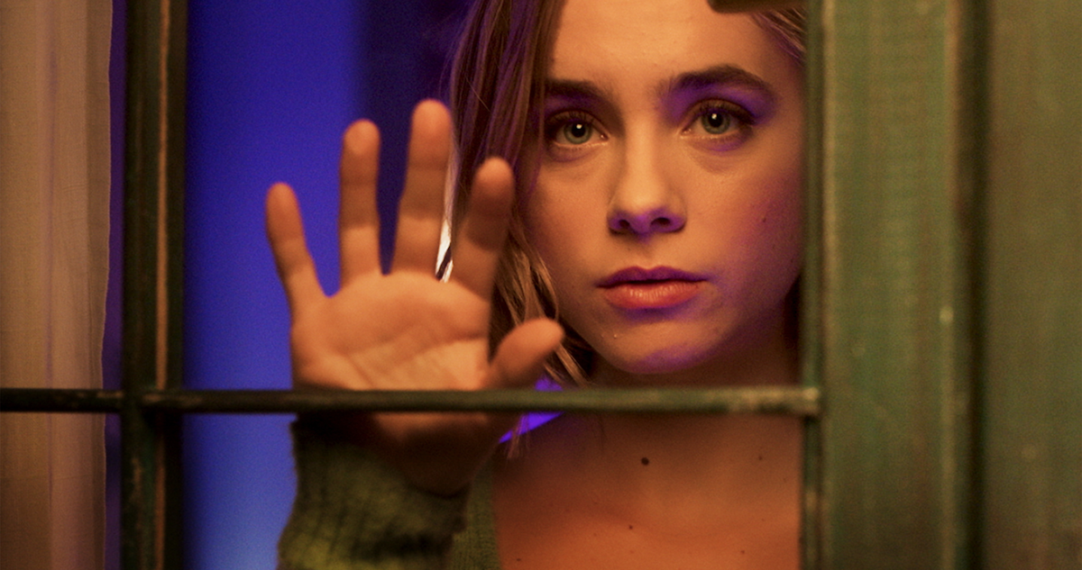 Close up of a young woman with blonde hair looking through a window.