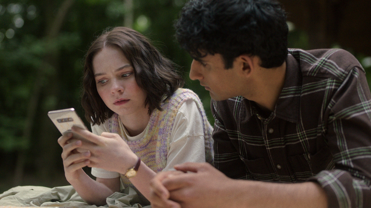 Emma Myers as Pip Fitz-Amobi and Zain Iqbal as Ravi Singh look at a phone with concerned expressions in Season 1 of ’A Good Girl’s Guide to Murder.’