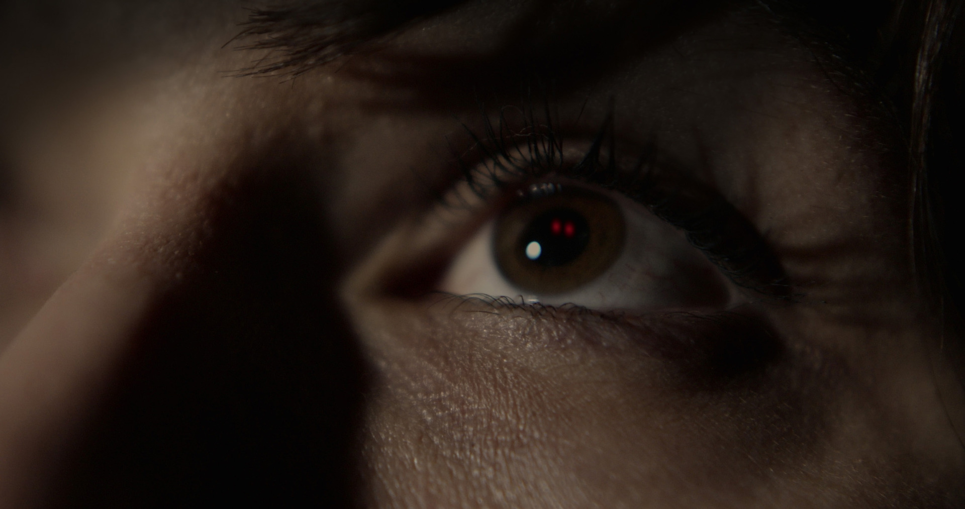 A red eyed figure is reflected into a woman's eyes.