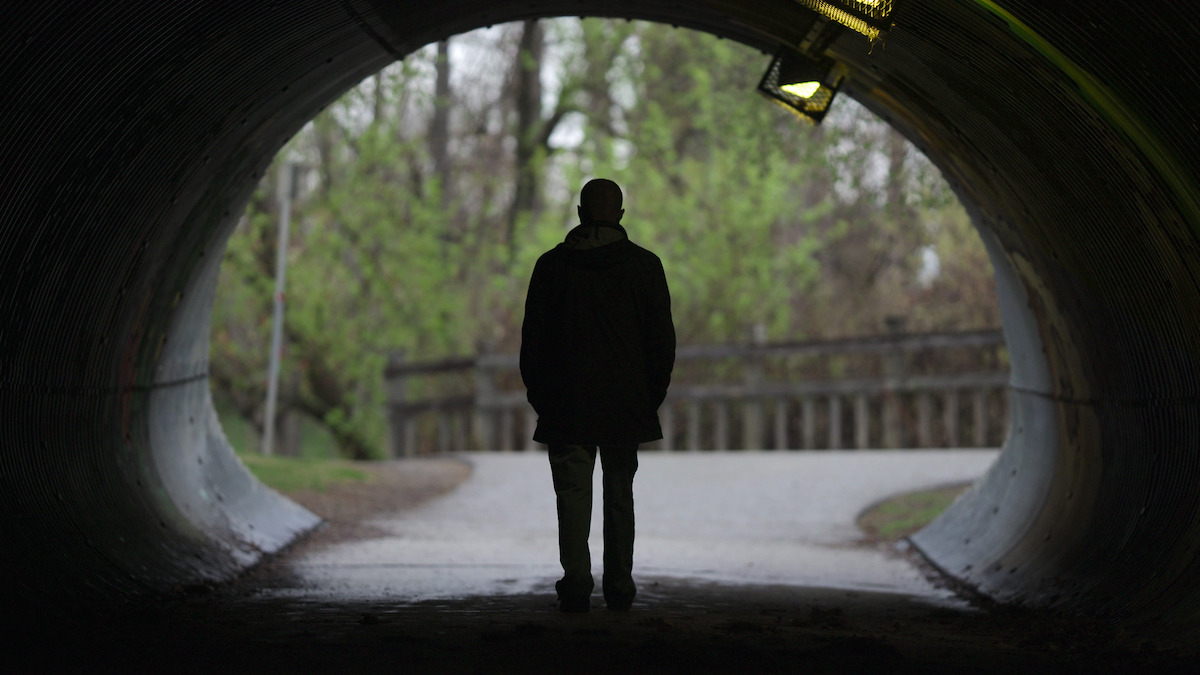 A silhouetted figure stands in a tunnel.