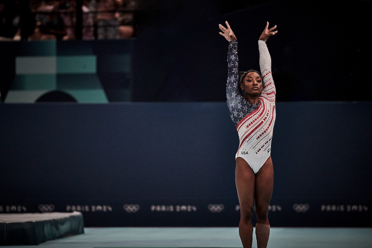 Simone Biles raises her hands triumphant after completing a routine.